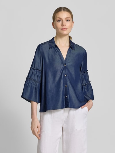 Frauenmodel trägt Regular Fit Jeansbluse aus Lyocell von s.Oliver BLACK LABEL in dunkelblauer Denim-Optik mit Frill, V-Ausschnitt, Hemdblusenkragen, einreihiger Knopfleiste und Trompetenärmeln, Ganzkörperansicht von vorne.