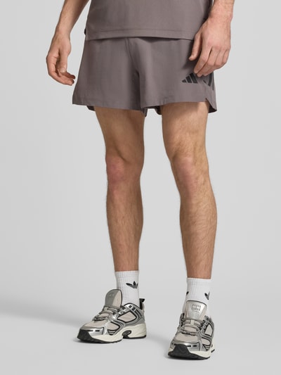 Męski model nosi Regular Fit Sport-Shorts mit elastischem Bund od adidas Training, jednolity kolor, krój regular fit, nadruk z logo, wstawka z siateczki, elastyczny pas, boczne wpuszczane kieszenie, Ganzkörperansicht z przodu.