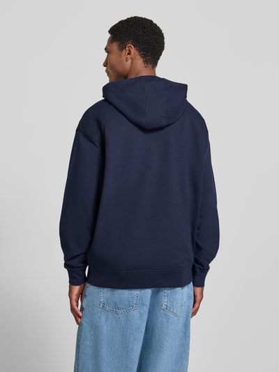 Mannenmodel draagt hoodie met labelprint en kangoeroezak van GUESS in donkerblauw katoenmix met stretch, regular fit, ruglengte 71 cm, mouwlengte 64 cm. Ganzkörperansicht Rückansicht.