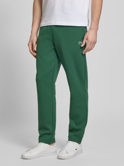 Mężczyzna nosi Tapered Sweatpants mit Baumwoll-Anteil od Lacoste Sport, zielony kolor, krój tapered, logo na nodze, widok z przodu, ujęcie całej sylwetki.