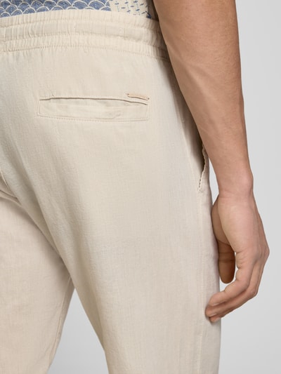 Mężczyzna nosi Hose aus Baumwoll-Leinen-Mix Modell 'KANE' von Jack & Jones, bawełniano-lniana, krój regular fit, elastyczny pas, szerokość w rozmiarze M 41 cm, długość nogawki od wewnątrz 81 cm, jasny beż, lekko teksturowany materiał, detal tylnej kieszeni, zbliżenie na tył
