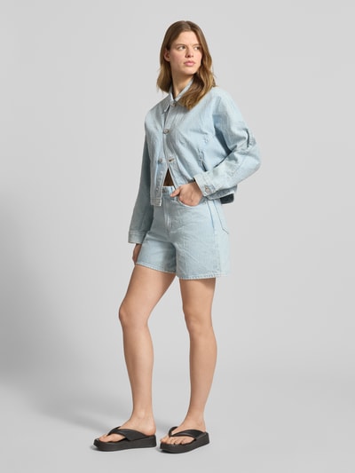 Frauenmodel trägt Jeansshorts im 5-Pocket-Design Modell '90S' von Calvin Klein Jeans in heller Jeans-Optik aus Reine Baumwolle, Wide-Fit, mit Knopf- und Reißverschluss, Label-Detail; Bundweite bei Größe 27: 40 cm, Innenbeinlänge: 14 cm, Ganzkörperansicht von vorne.