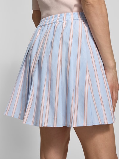 Frauenmodel trägt Ausgestellter Faltenrock aus reiner Baumwolle von Lacoste, gestreift in Blau und Rosa, Popeline, Mini-Länge, Ganzkörperansicht Rückansicht.