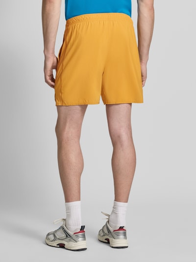 Mężczyznę model prezentuje Regular Fit Shorts mit integriertem Slip Modell 'Core' od ASICS TIGER w kolorze żółtym, elastyczny pas, nadruk z logo, szerokość w rozmiarze M: 38 cm, długość wewnętrzna nogawki w rozmiarze M: 17 cm, widok całej sylwetki z tyłu.