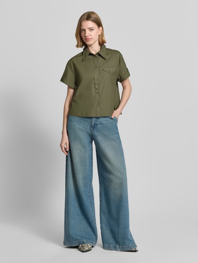 Frauenmodel trägt Boxy Fit Bluse mit Brusttasche von Luisa Cerano aus reiner Baumwolle, olivgrün, breite Passform, Knopfleiste, Brusttasche, gerade geschnittene Kurzarm-Ärmel mit Aufschlag, kombiniert mit weiter Jeans, Ganzkörperansicht von vorne.