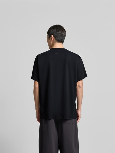 Männermodel trägt Relaxed Fit T-Shirt mit Logo-Detail von MM6 Maison Margiela in Schwarz, reine Baumwolle, Rückenansicht, Ganzkörperansicht Rückansicht.
