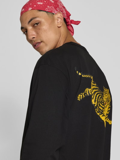 Männermodel trägt Longsleeve aus reiner Baumwolle von Kenzo in zwart met gele labelprint, regular fit, ruglengte maat M 70 cm, rugaanzicht