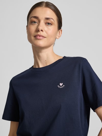 Modelka kobieca nosi Regular Fit T-Shirt aus reiner Baumwolle od s.Oliver RED LABEL, efekt: jednolity kolor, aplikacja: haft, okrągły dekolt, krótki rękaw, materiał: bawełna, kolor granatowy, widok z przodu, zbliżenie na górną część ciała.