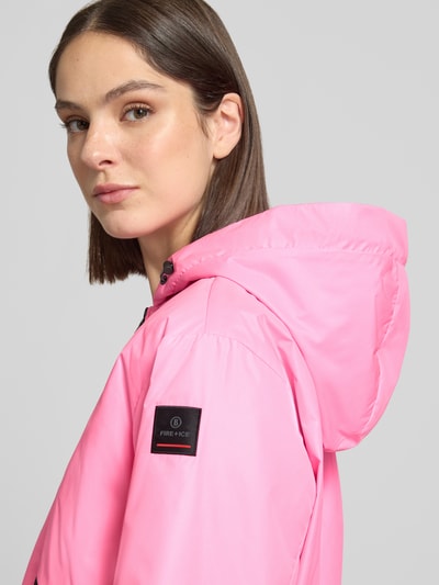 Modelka kobieca nosi kurtkę Jacke mit Reißverschlusstaschen Modell 'YADIRA' od FIRE + ICE, róż, kaptur, krój regular fit, zamek błyskawiczny dwustronny, kieszenie zapinane na zamek błyskawiczny, długość tyłu w rozmiarze 36: 52 cm, szerokość ramion w rozmiarze 36: 45 cm, szerokość klatki piersiowej w rozmiarze 36: 45 cm, długość rękawów w rozmiarze 36: 61 cm, zbliżenie na górną część ciała z przodu.