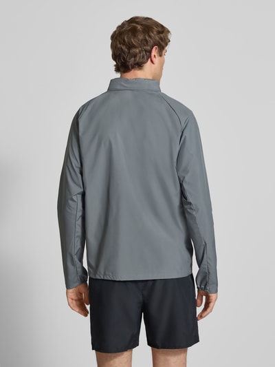 Männermodel trägt Regular Fit Jacke mit Stehkragen Modell 'Miler' von NIKE TRAINING in Grau mit Logo-Print, Ganzkörperansicht Rückansicht.