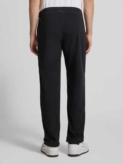 Männermodel trägt Sweatpants mit elastischem Bund von CHAMPION in Schwarz, Label-Stitching, lockerer Schnitt, Ganzkörperansicht Rückansicht.