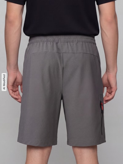 Männermodel trägt Regular Fit Sportshorts mit Label-Print von PUMA Performance in Grau, lockerer Schnitt, glatte Textur, Ganzkörperansicht Rückansicht.