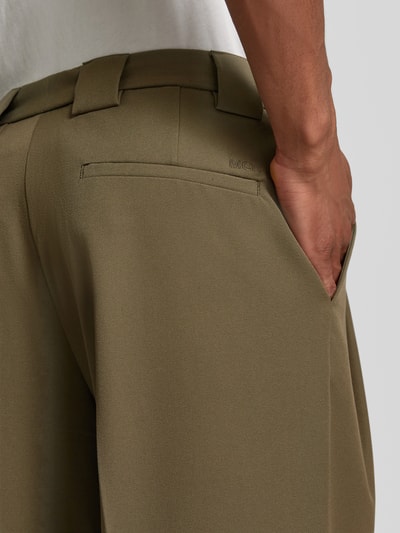Männermodel trägt Stoffhose mit Bügelfalten und Eingrifftaschen von MCNEAL, olivegrüner Material-Mix mit Viskose-Anteil, Detailaufnahme Rückansicht. Kontext: Loose-Fit, Knopf-Reißverschluss, französische Eingrifftaschen, Gesäßleistentaschen, Bundweite 34 cm, Innenbeinlänge 80 cm bei Größe 50.