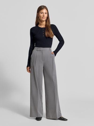Kobieta modelka nosi Slim Fit Longsleeve aus Strick-Optik od MYON, czarny, imitacja dzianiny, krój slim fit, listwa guzikowa, okrągły dekolt, długość tyłu w rozmiarze 36 to 60 cm, długość rękawów w rozmiarze 36 to 66 cm, prosty splot, gładka faktura, widoczne szare spodnie, całkowity widok z przodu.