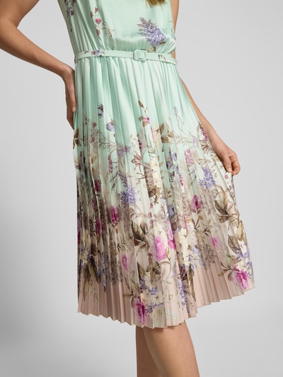 Frauenmodel trägt Knielanges Cocktailkleid mit Plisseefalten von Rinascimento, floraler Allover-Look in Pastell, A-Linie, Nahaufnahme Unterkörper.