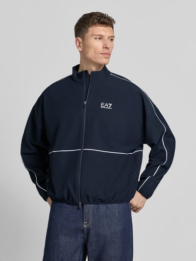Männermodel trägt dunkelblaue Bomberjacke mit Stehkragen, Logo-Print und weißen Details, VENTUS7-Gewebe, Ganzkörperansicht von vorne. Produktname: Bomberjacke mit Stehkragen und Logo-Print von EA7 Emporio Armani, gerader Schnitt, Zweiwege-Reißverschluss, elastische Abschlüsse.