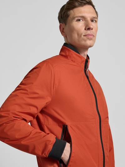 Männermodel trägt Regular Fit Jacke mit Stehkragen von MCNEAL in Orange mit Reißverschluss und elastischen Abschlüssen, Nahaufnahme Oberkörper.