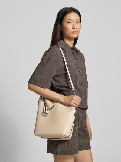 Frauenmodel trägt Hobo Bag mit Logo-Prägung Modell 'LOHJA' von Seidenfelt in Beige, grobe Textur, verstellbarer Schultergurt, Hauptfach mit Magnetverschluss, Anhänger mit Logo-Detail, Reißverschlussfach innen, Breite 30 cm, Länge 29 cm, Tiefe 13 cm, Länge Schulterriemen 84 cm, Ganzkörperansicht von vorne.