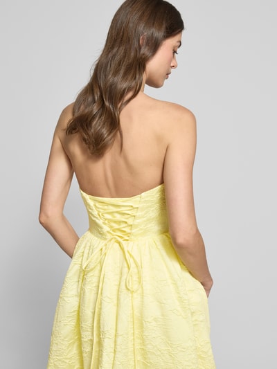 Frauenmodel trägt Minikleid mit floralem Allover-Stitching von Hey Kyla in Pastellgelb, tailliert, schulterfrei, Rückenansicht, Detailaufnahme.