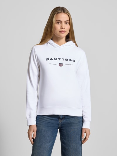 Vrouwenmodel draagt Regular Fit Hoodie met Labelprint van Gant, katoenmix, wit met zwarte print, regular fit, labelprint, voorkant, Ganzkörperansicht von vorne.
