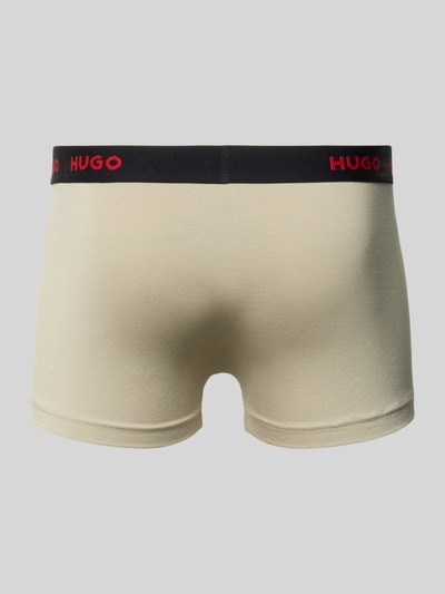 Männermodel trägt Trunk aus Baumwoll-Mix im 3er-Pack von HUGO für Herren in Beige mit schwarzem Bund und rotem Logo, Ganzkörperansicht Rückansicht.