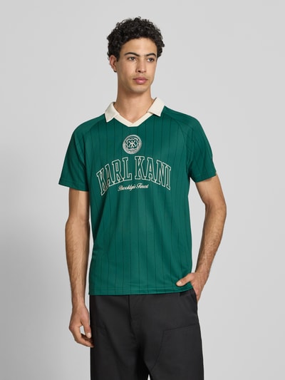 Männermodel trägt Regular Fit T-Shirt mit Umlegekragen von KARL KANI in Grün mit Logo-Stitching, Rückenlänge 67 cm, Ganzkörperansicht von vorne.