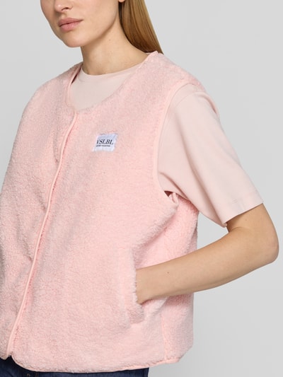 Frauenmodel trägt Regular Fit Weste in Teddy-Optik Modell 'AMALIA' von VILLA SOPHIE in zartem Rosa mit Druckknopfleiste, Label-Patch, seitlichen Eingrifftaschen und weicher Teddyfell-Materialverarbeitung, Nahaufnahme Oberkörper.
