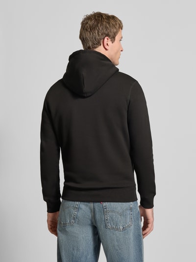 Männermodel trägt Hoodie mit Känguru-Tasche von REVIEW aus schwarzer Baumwollmischung, Slim-Fit, elastische Abschlüsse, Ganzkörperansicht Rückansicht.
