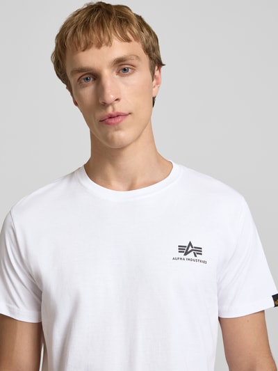 Mannenmodel draagt T-Shirt met Logo en Rundhalsausschnitt van Alpha Industries in wit, regular fit, zuiver katoen, Nahaufnahme bovenlichaam.