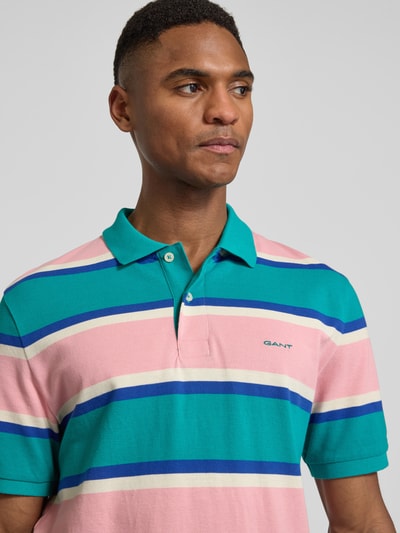 Männermodel trägt Slim Fit Poloshirt mit Logo-Stitching von Gant in rosa, grün und blau aus Bio-Baumwolle, Nahaufnahme Oberkörper.