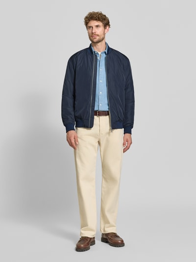 Männermodel trägt Regular Fit Bomberjacke mit Baseball-Kragen Modell 'CHARLES' von Selected in Dunkelblau, kombiniert mit heller Hose, Herren Bomberjacke, Ganzkörperansicht von vorne.