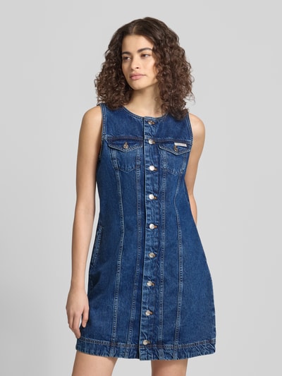 Vrouwenmodel draagt Regular Fit Minikleid in Denim-Optik mit Logo-Patch van Calvin Klein Jeans, katoen, mouwloos, ronde hals, borstzakken, steekzakken, blauwe denimlook, voorkantaanzicht bovenlichaam.