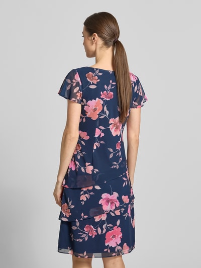 Frauenmodel trägt knielanges Cocktailkleid mit Wasserfall-Ausschnitt von Christian Berg Cocktail aus Chiffon, Taillierter Schnitt, Schmetterlingsärmel, Rock mit Drapierungen, Rückenlänge bei Größe 36: 97 cm, Brustweite: 46 cm, Ärmellänge: 16 cm, florales Muster in Blau und Pink, Ganzkörperansicht Rückansicht.