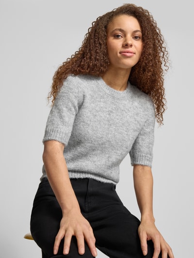 Vrouwenmodel draagt Regular Fit Strickpullover mit Woll-Anteil Modell 'STARLA' van Only, effen lichtgrijs melange, ronde hals, korte mouw, geribde boorden, breisel, frontale close-up bovenlichaam.