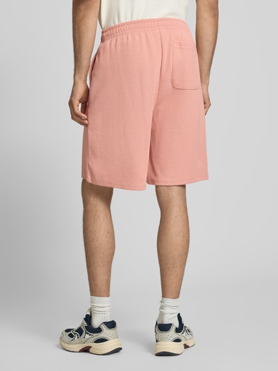 Männermodel trägt Regular Fit Shorts mit Strukturmuster von KARL KANI in Rosa aus Baumwoll-Mix mit Logo-Stitching, Ganzkörperansicht Rückansicht.