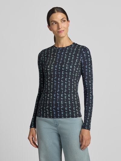 Frauenmodel trägt Longsleeve mit Label-Print von Marc Cain, Material-Mix mit Stretch-Anteil, dunkelblau mit Muster, Ganzkörperansicht von vorne.