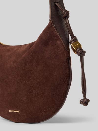Produktfoto, Handtasche aus echtem Leder Modell 'MOON' von Coccinelle in Dunkelbraun, samtige Textur, goldene Label-Details, Nahaufnahme