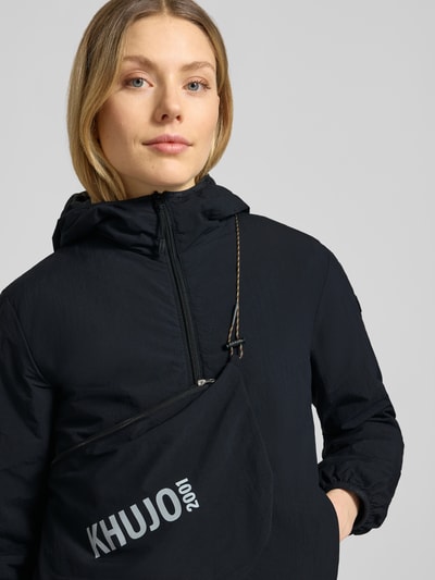 Vrouwenmodel draagt zwarte dames jack met capuchon, ritssluitingdetail, labeldetail, model 'SHELLY2' van khujo, regular fit, nahaufnahme oberkörper. Ruglengte maat S: 56 cm, schouderbreedte: 52 cm, borstwijdte: 46 cm, mouwlengte: 52 cm.