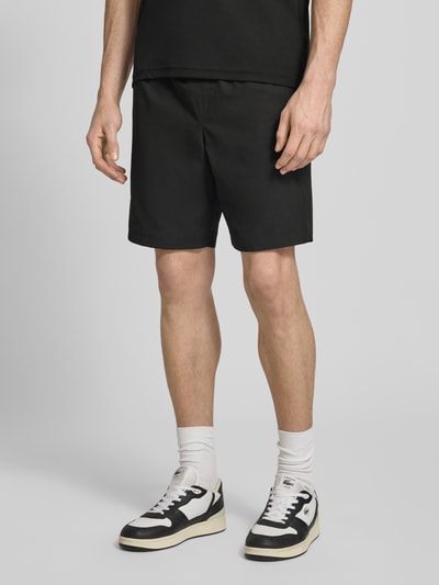 Männermodel trägt Relaxed Fit Sport-Shorts mit Logo-Stitching von Lacoste Sport in Schwarz, seitliche Eingrifftaschen, unifarbene Optik, Ganzkörperansicht von vorne