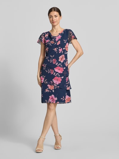 Frauenmodel trägt Knielanges Cocktailkleid mit Wasserfall-Ausschnitt von Christian Berg Cocktail aus blauem Chiffon, florales Muster, Taillierter Schnitt, Schmetterlingsärmel, Rock mit Drapierungen, Größe 36: Rückenlänge 97 cm, Brustweite 46 cm, Ärmellänge 16 cm, Ganzkörperansicht von vorne.