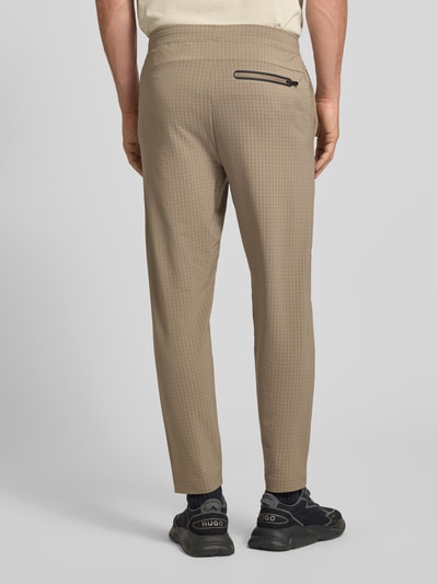 Männermodel trägt Tapered Fit Hose mit Waffelstrukturmuster Modell 'TERRACE' von BOSS Green in Beige mit elastischem Bund, Ganzkörperansicht Rückansicht.