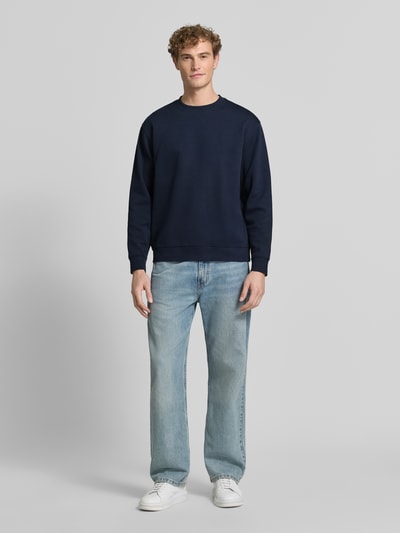 Männermodel trägt dunkelblauen slim fit pullover aus pure katoen 'TOM' van Selected, heren sweatshirt, lichte spijkerbroek, witte sneakers, ganzkörperansicht van voren