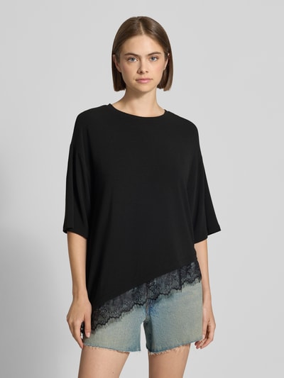 Frauenmodel trägt schwarzes T-Shirt Modell 'GLAMOUR' von ONLY mit Spitzenbesatz, kombiniert mit hellblauen Jeansshorts, Ganzkörperansicht von vorne. Damen T-Shirt von ONLY