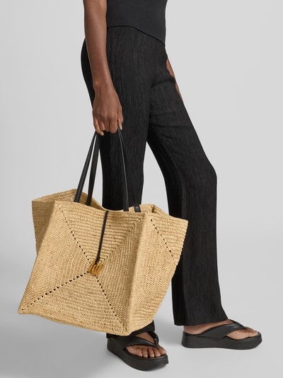 Frauenmodel trägt Tote Bag in Flecht-Optik von Nanushka aus Reinem Bast mit schmalen Schulterriemen, rechteckige Form, Naturton, schwarze Riemen, herausnehmbare Innentasche mit Reißverschluss, Maße 34 cm Breite, 34 cm Länge, 34 cm Tiefe, Ganzkörperansicht von vorne.