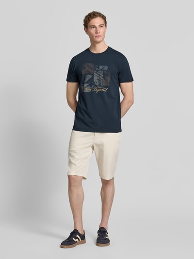Männermodel trägt dunkelblaues Herren T-Shirt mit Label-Print und Rundhalsausschnitt von PME Legend aus Reine Baumwolle, Regular-Fit, kombiniert mit hellen Shorts und Sneakers, Rückenlänge bei Größe M 72 cm, Ganzkörperansicht von vorne.