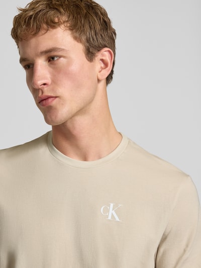 Männermodel trägt Regular Fit T-Shirt mit Logo-Print von Calvin Klein Jeans in Beige, reine Baumwolle, Nahaufnahme Oberkörper.