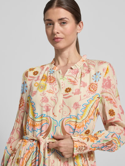Frauenmodel trägt Regular Fit Kleid mit floralem Allover-Print von HERZENS in Beige mit bunten Blumenmotiven, Stehkragen, Tailliert, Langärmelig, elastische Ärmelabschlüsse, abnehmbares Stoffband und Knopfleiste, Nahaufnahme Oberkörper.