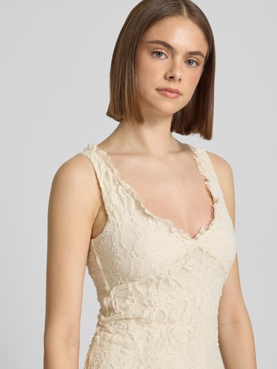 Frauenmodel trägt schmales Spitzenkleid mit tiefem V-Ausschnitt Modell 'ALBINA' von Only in Creme, geprägt von floraler Struktur, Nahaufnahme Oberkörper.