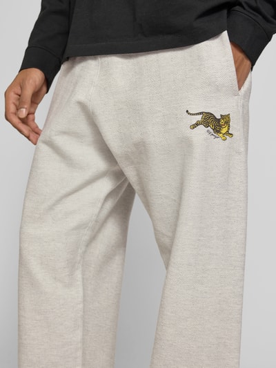 Mannelijk model draagt Sweatpants aus Baumwoll-Mix van Kenzo in lichtgrijs met labelprint, steekzakken, los model, mix van katoen en elastaan, binnenbeenlengte maat M 81 cm, bandwijdte maat M 37 cm, detailopname heup.