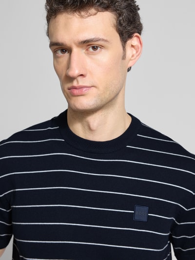 Männermodel trägt Regular Fit T-Shirt aus Baumwoll-Kaschmir-Mix Modell 'KANACHO' von BOSS Orange, dunkelblau mit weißen Streifen, Stricktextur, Label Patch, Rundhals, Nahaufnahme Oberkörper.